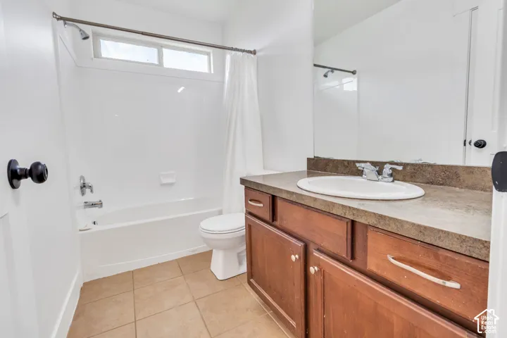 Vanity with an integrated sink and wood-finish cabinetry, full-width mirror, tile flooring, and a shower-tub combination with an overhead window