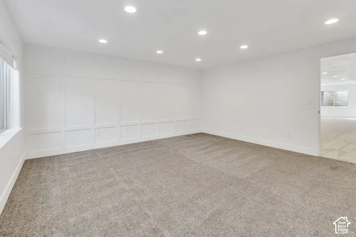 Recessed lighting, wall paneling, light gray carpeting, and white painted walls