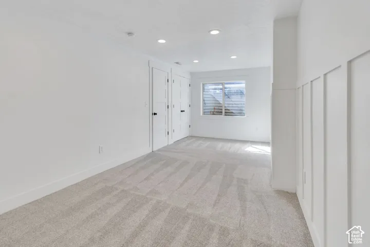 Recessed lighting illuminating a spacious room with light gray carpet, white walls, white trim, and a window with blinds