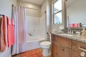 Bathroom featuring a wood-finish vanity with a stone countertop, an integrated sink, a large wall-mounted mirror, and a bathtub with shower