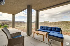 Covered patio with concrete flooring, supported by substantial columns, overlooking a natural landscape