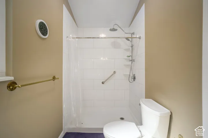 White subway tile shower with a handheld showerhead, built-in shelving, and a safety grab bar