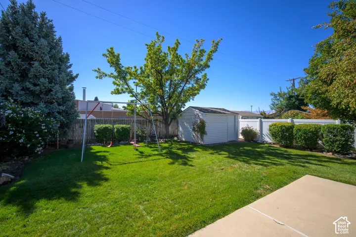 Expansive green lawn, mature trees, concrete patio area, white privacy fencing, and a storage shed