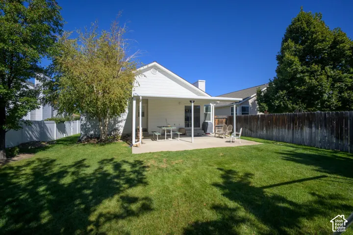 Expansive backyard featuring a manicured lawn, established trees, and a concrete patio with an attached awning