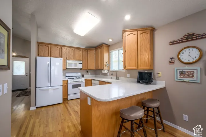 Kitchen featuring wood-finish flooring, light wood cabinetry, white countertops, and white appliances
