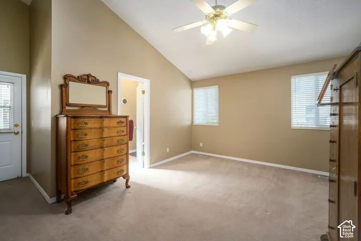 Vaulted ceiling with a ceiling fan, dual windows with blinds, and neutral carpeting