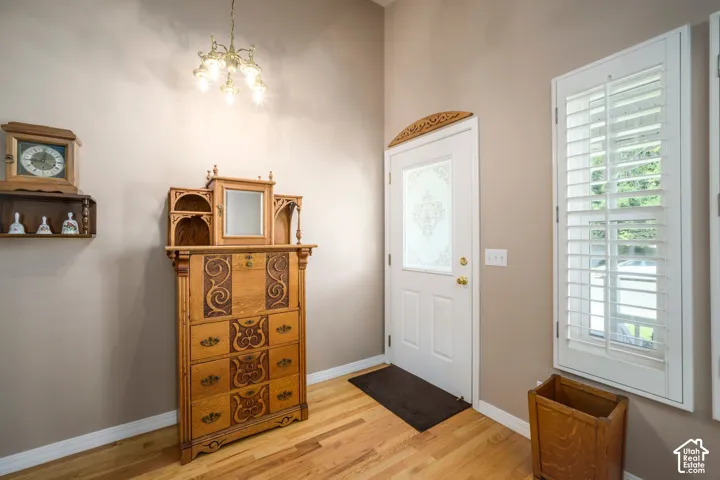 Hardwood flooring, decorative glass paneled entry door, window with plantation shutters, and a brass chandelier
