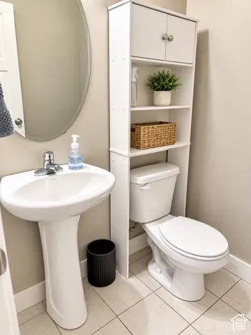 Pedestal sink with chrome fixtures, oval mirror, and tiled flooring