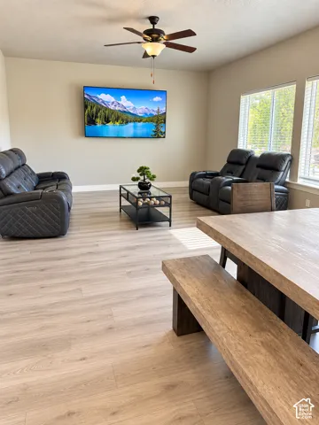 Expansive living area featuring light wood-finish flooring, a contemporary ceiling fan with integrated lighting, and multiple windows