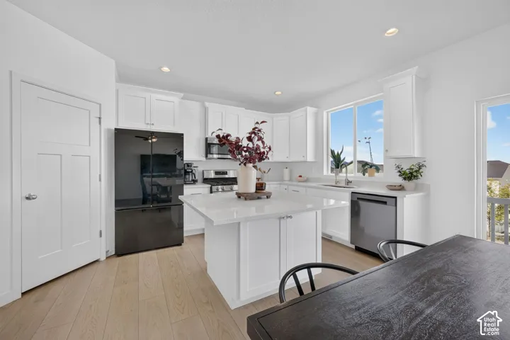Kitchen featuring white cabinetry, light wood-finish flooring, a central island with a light-toned countertop, stainless steel appliances, and abundant natural light