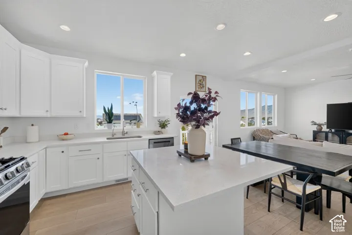 White shaker cabinetry, light-toned wood-finish flooring, recessed lighting, and a kitchen island with a light-colored countertop