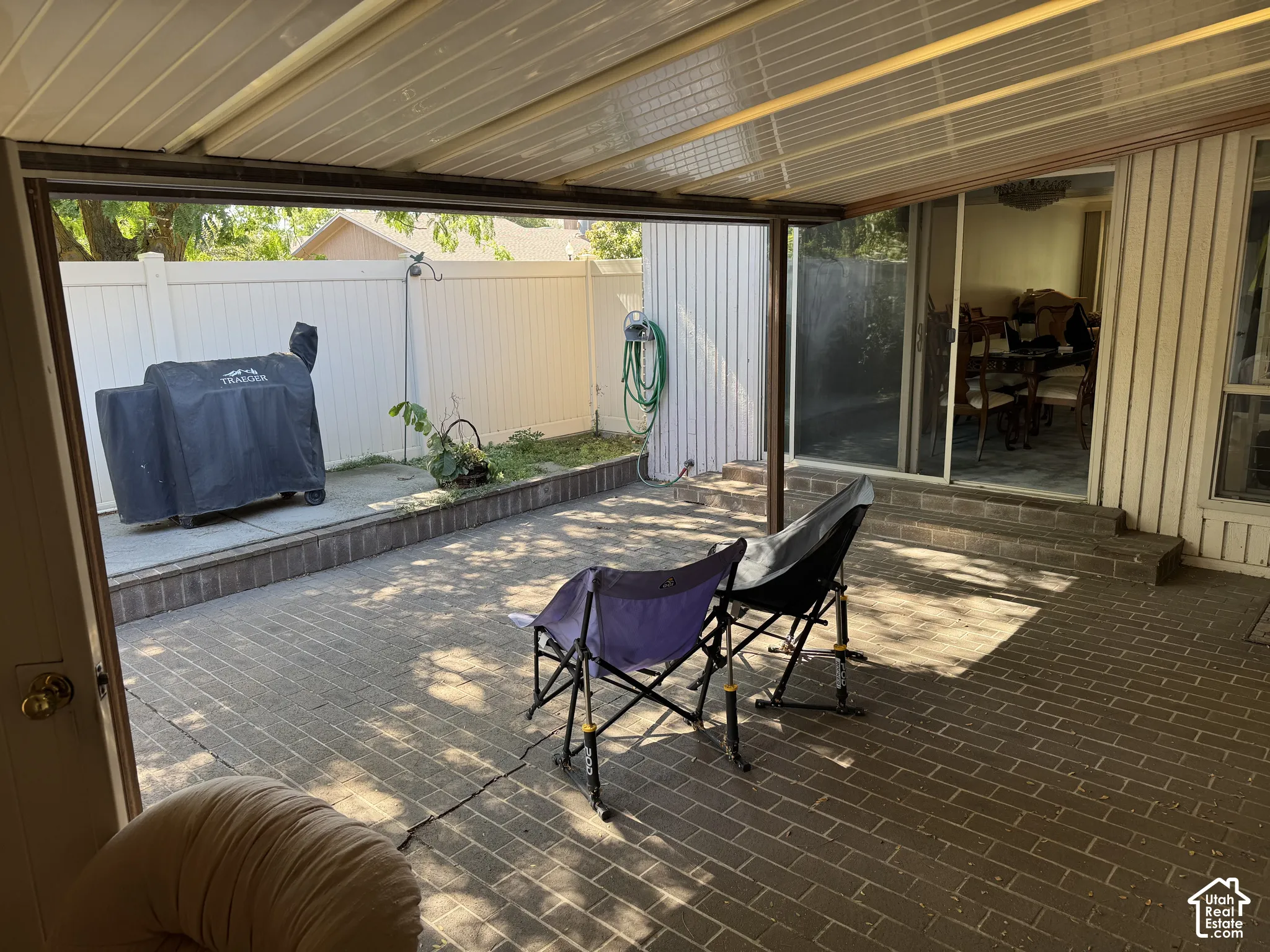 Brick-paver patio with a covered overhead structure, perimeter fencing, and raised planting beds