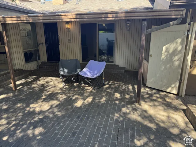 Paved patio area with a covered extension, exterior lighting fixtures, and a sliding glass door entry