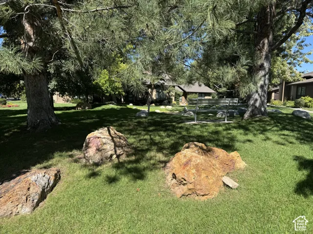 Expansive lawn area featuring mature trees, natural rock formations, and a metal park bench