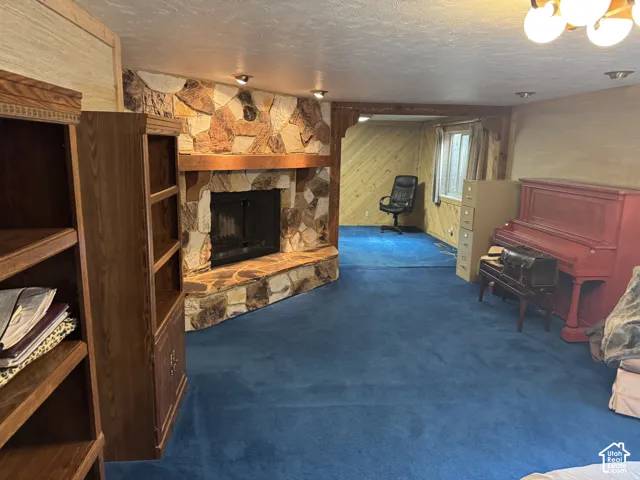 Stone-clad fireplace with a wood mantel, built-in wooden shelving, blue carpeting, and wood-paneled walls