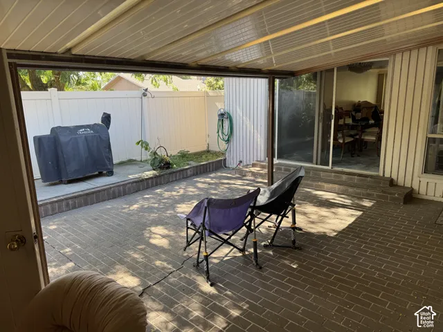 Brick-paver patio with a covered overhead structure, perimeter fencing, and raised planting beds