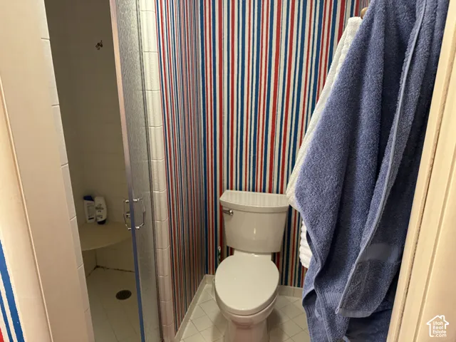 Enclosed shower with glass door and built-in seat, white tiled flooring, and a toilet