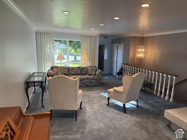 Recessed lighting throughout, crown molding, large picture window with drapes, staircase with wood handrail and white balusters, and a chandelier