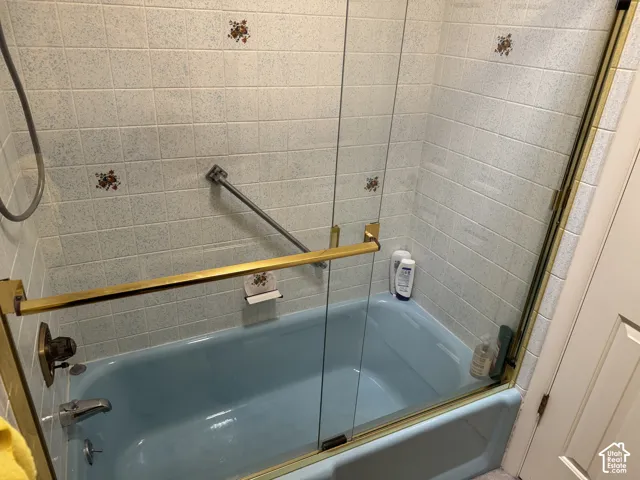 Bathtub with a glass shower enclosure, brass-finish hardware, and tiled surround