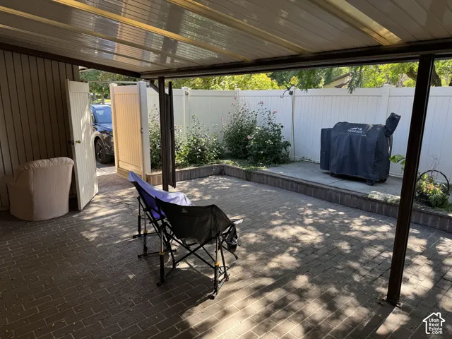 Covered patio featuring a translucent roof, paver flooring, privacy fencing, and a side gate