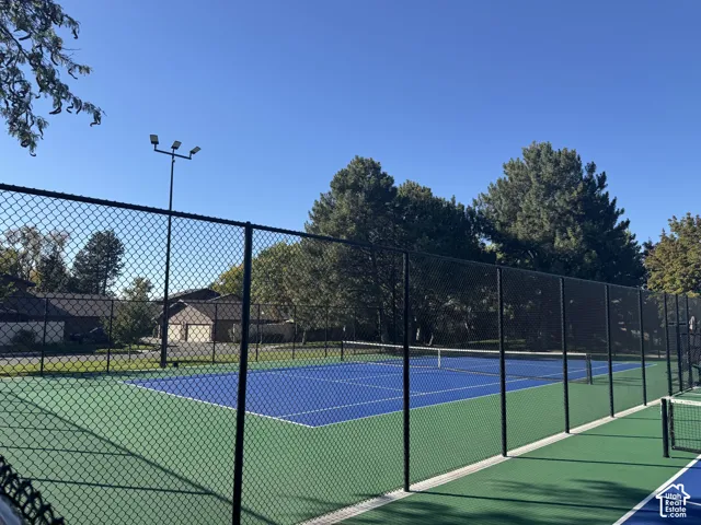 Full-size tennis court featuring a blue playing surface and green surrounding area