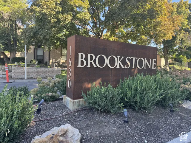 Brookstone entry sign with address numbers, surrounded by established landscaping, and illuminated by ground-level accent lighting