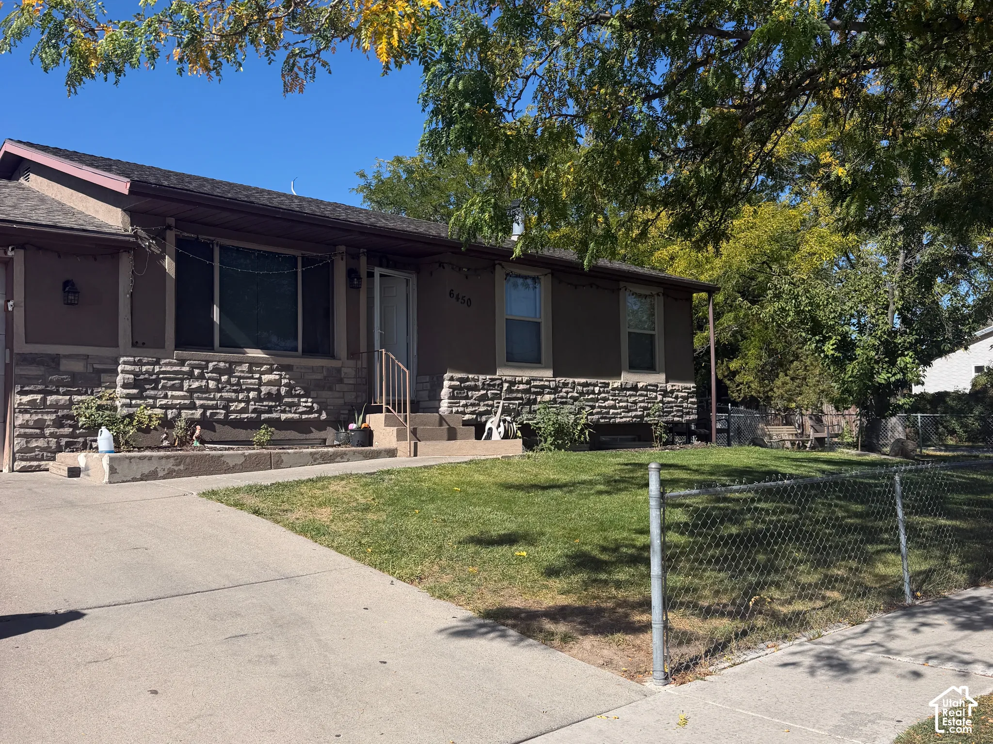 Exterior with a stone facade, stucco siding, a concrete driveway, and a chain-link fence