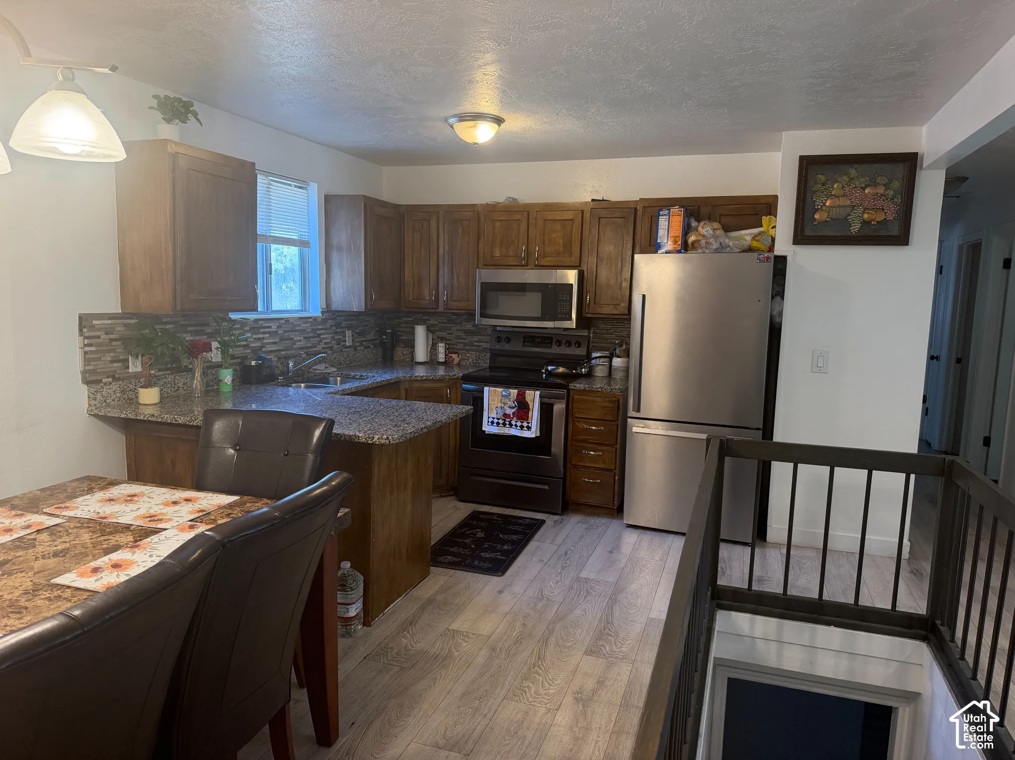 Kitchen featuring wood-finish cabinetry, granite-style countertops, stainless steel appliances, a tiled backsplash, and light wood-finish flooring