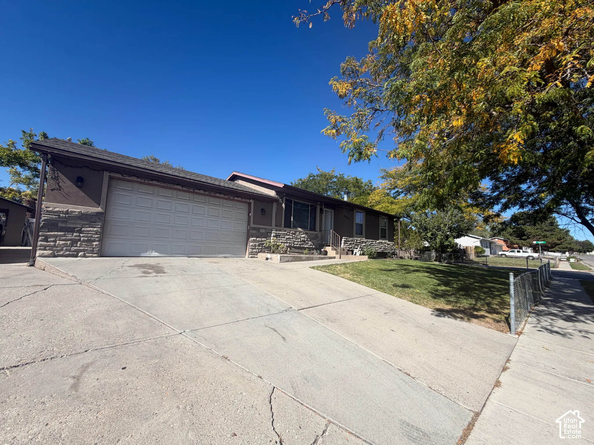 Attached two-car garage with a concrete driveway, stone exterior accents, and mature trees
