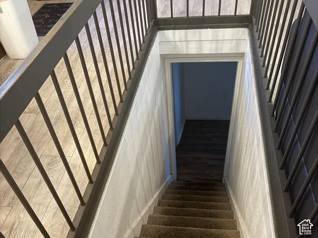 Stairwell featuring carpeted treads, vertical slat railing, and light-tone wood-finish flooring at the landing