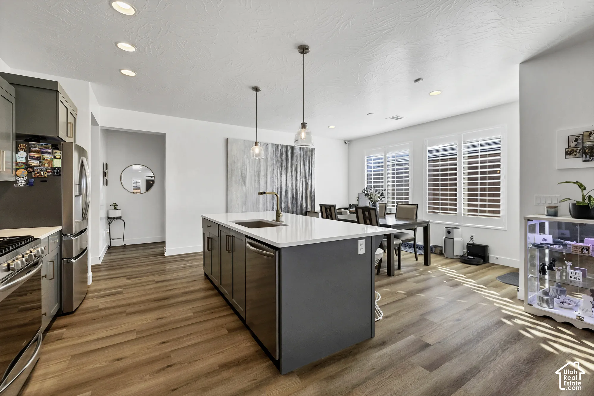 Kitchen featuring a center island with a sink, stainless steel appliances, wood-finish flooring, recessed lighting, and pendant lighting