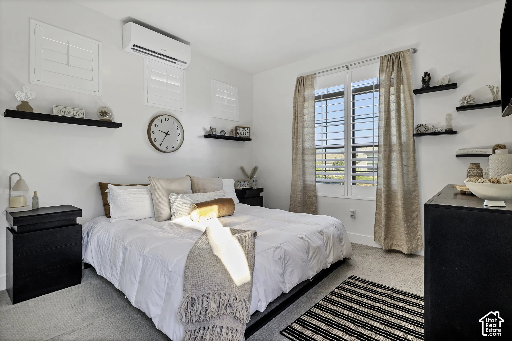 Casita window with louvered shutters, wall-mounted air conditioning unit, built-in shelving, light gray carpeting, and white walls