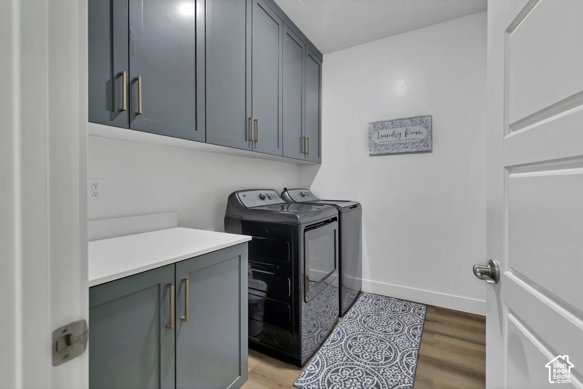 Laundry area featuring dark gray cabinetry with gold-tone hardware, a white countertop, and wood-finish flooring