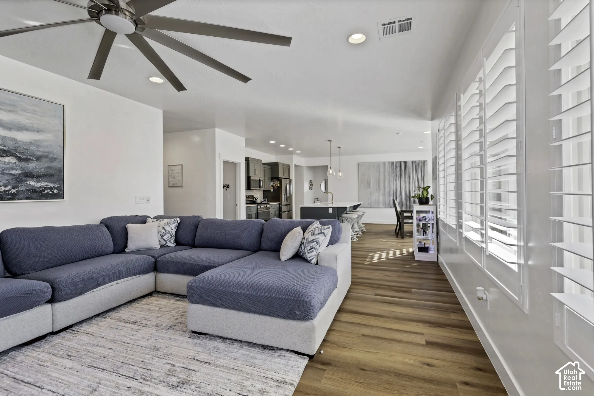 Spacious living area featuring wood-finish flooring, recessed lighting, a modern ceiling fan, and plantation shutters