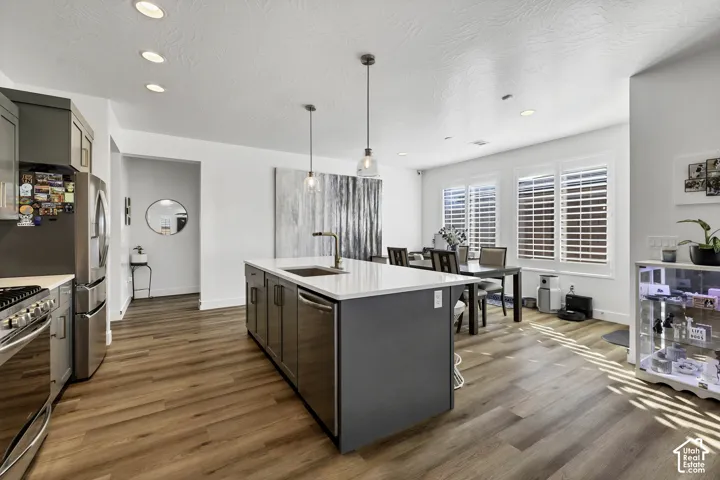 Kitchen featuring a center island with a sink, stainless steel appliances, wood-finish flooring, recessed lighting, and pendant lighting
