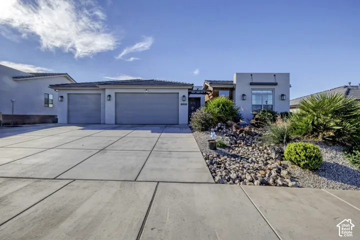 Two-car garage with overhead doors, expansive concrete driveway, and desert-inspired landscaping