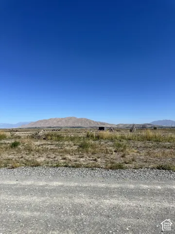 Expansive land parcel with distant mountain backdrop, featuring a gravel road frontage and natural vegetation