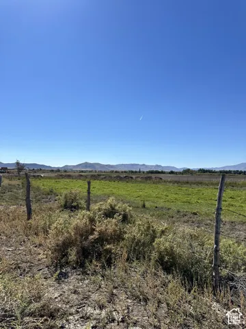 Expansive rural landscape featuring a green field and distant mountains under a clear sky