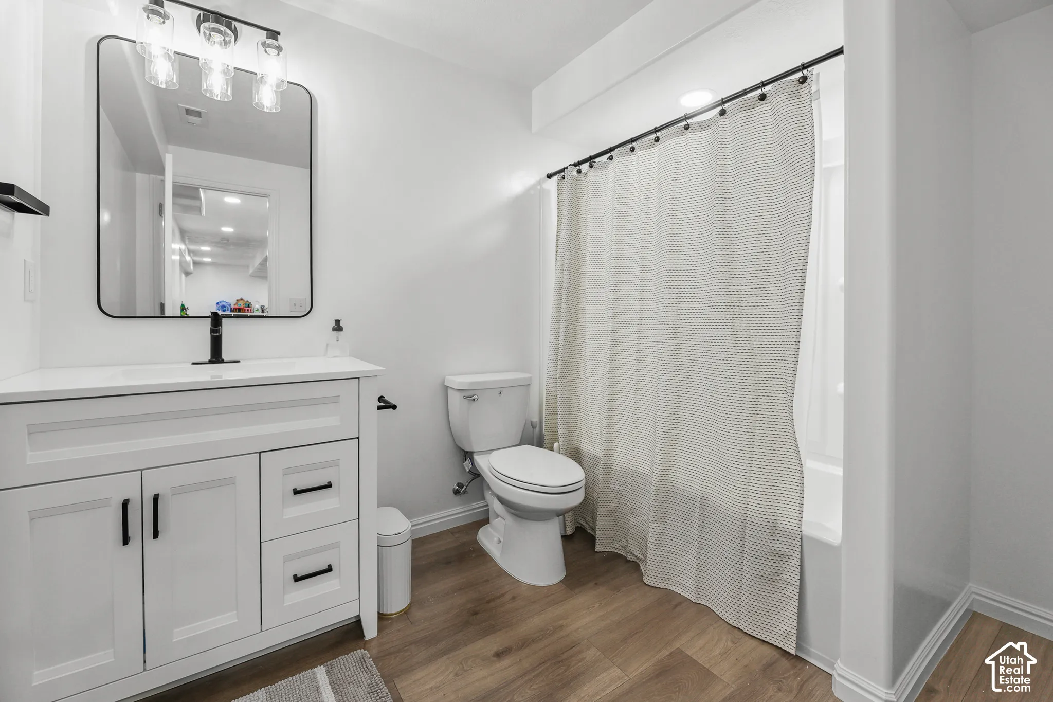 White vanity with black hardware, wood-finish flooring, and a shower-tub combination