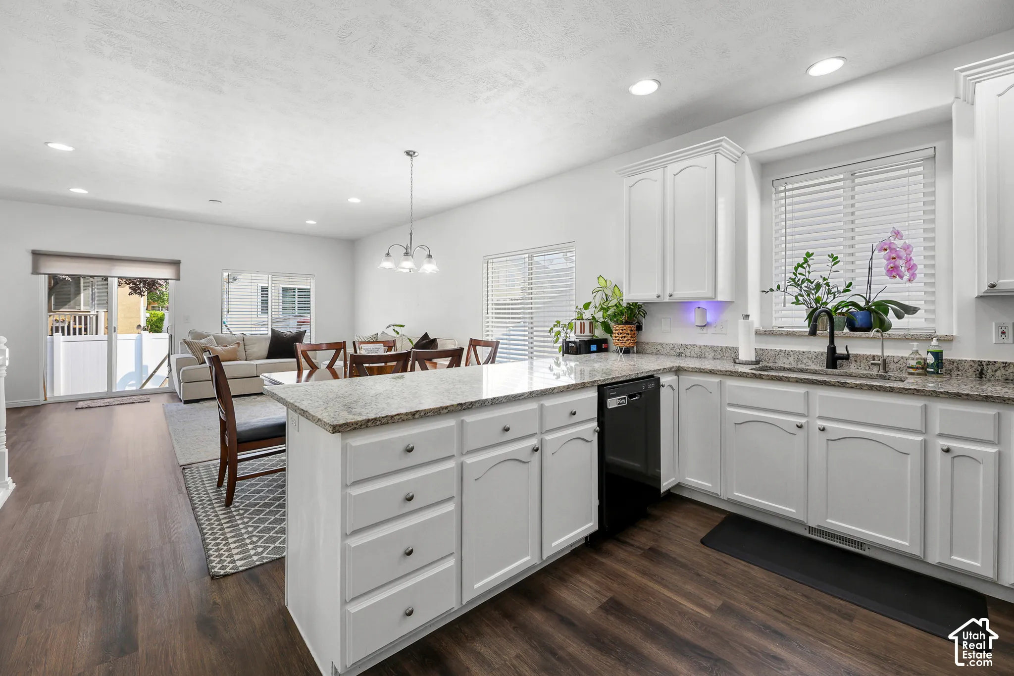 Kitchen featuring white cabinetry, light-toned countertops, a black dishwasher, and dark wood-finish flooring