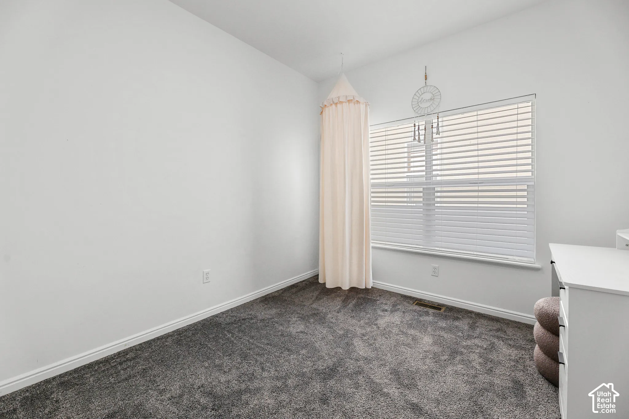 Bright bedroom showcasing neutral wall finishes, plush carpeting, and large windows with horizontal blinds and sheer curtains providing natural light
