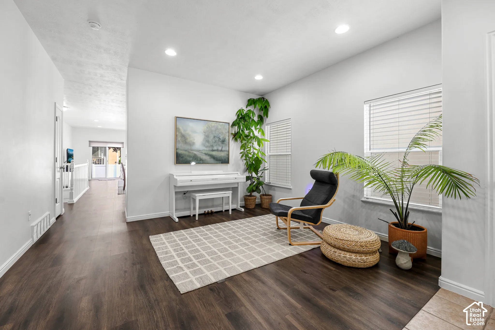 Bright, open living space showcasing dark wood-finish flooring, recessed ceiling lighting, and large windows with plantation shutters