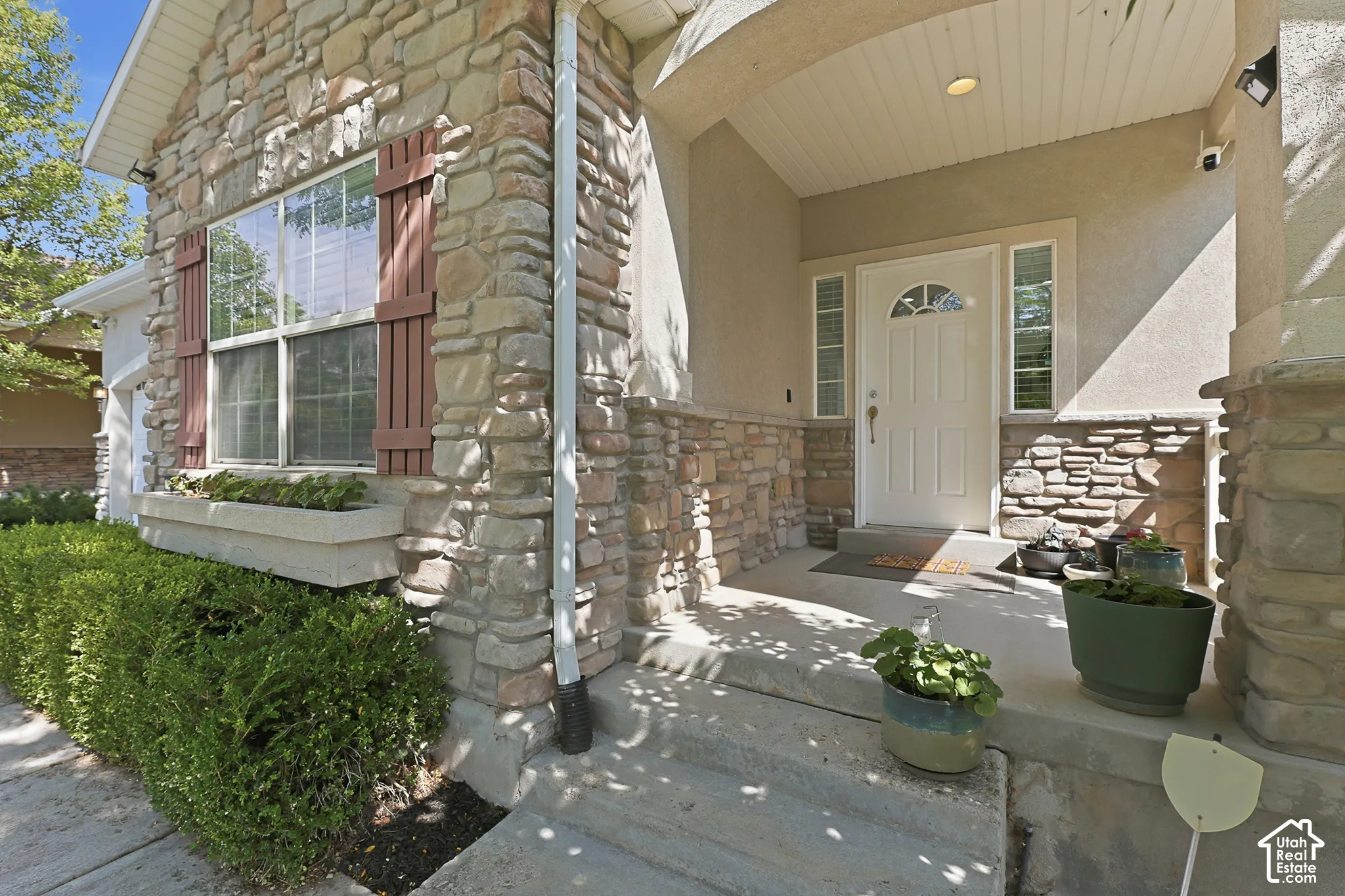 Stone and stucco exterior with a covered front entry featuring a white painted door, sidelight windows, and decorative stone accents
