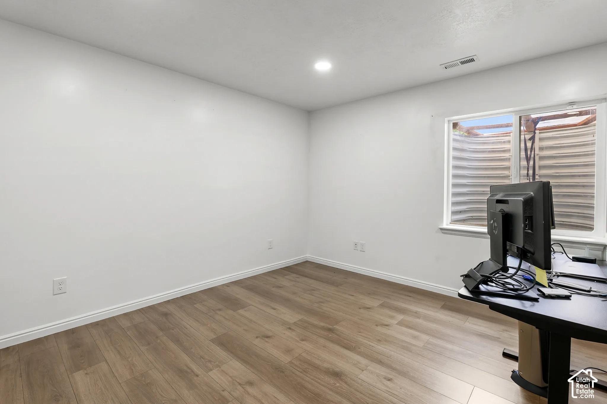 Bright, light-filled office space featuring pristine white walls, recessed ceiling lighting, and wood-finish flooring throughout