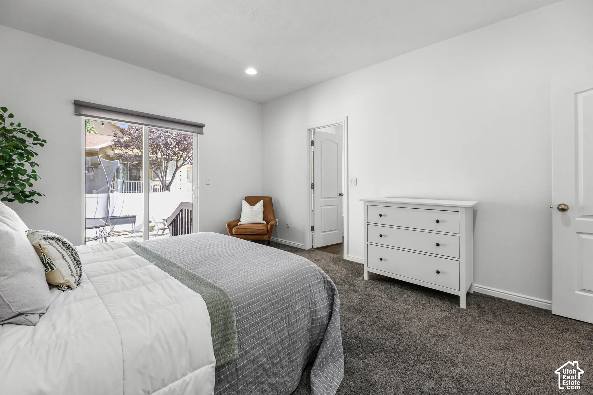 Bright secondary bedroom featuring dual beds, abundant natural light from sliding glass doors opening to a private balcony, carpeted flooring, white painted walls, a white dresser with multiple drawers, and direct access to an ensuite bathroom with glass-