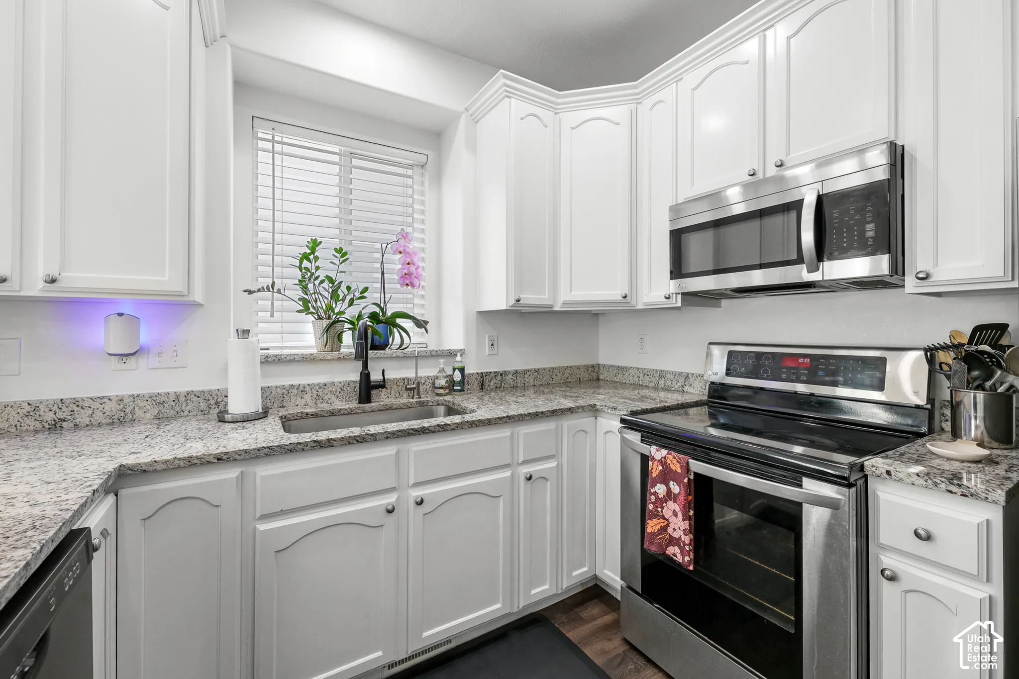 White cabinetry with silver-tone hardware, stainless steel appliances, speckled stone countertops, undermount sink with a matte black faucet, and wood-finish flooring
