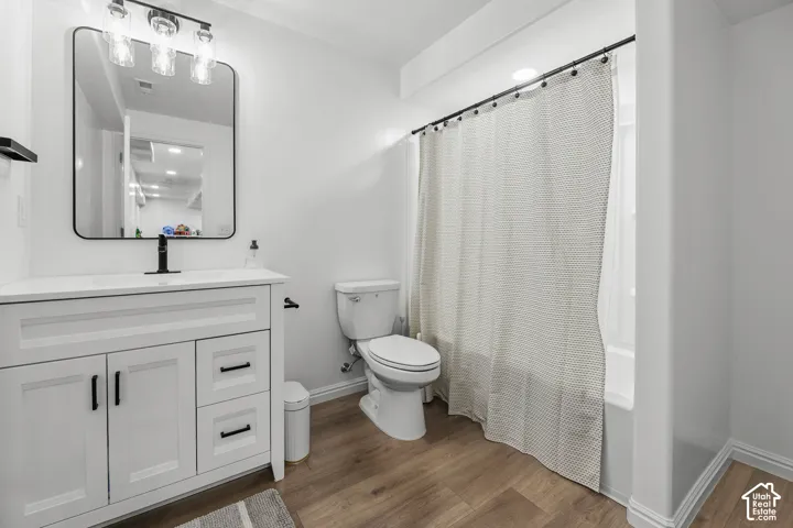 White vanity with black hardware, wood-finish flooring, and a shower-tub combination