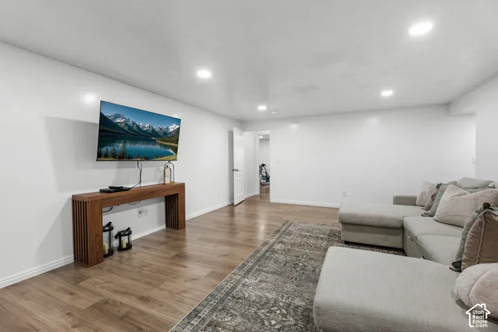 Modern recreation room featuring warm wood-finish flooring, recessed ceiling lighting, and a wall-mounted flat-screen television above a wooden console table