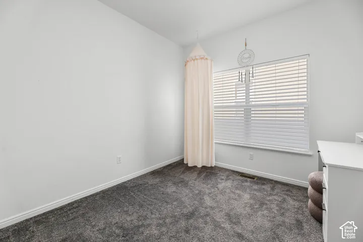Bright bedroom showcasing neutral wall finishes, plush carpeting, and large windows with horizontal blinds and sheer curtains providing natural light