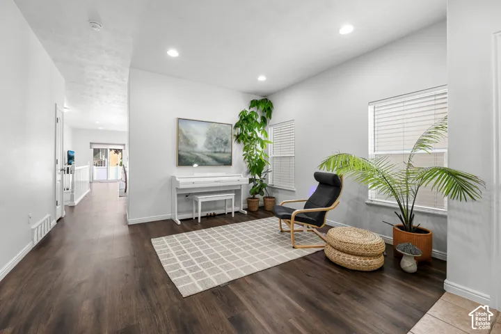 Bright, open living space showcasing dark wood-finish flooring, recessed ceiling lighting, and large windows with plantation shutters